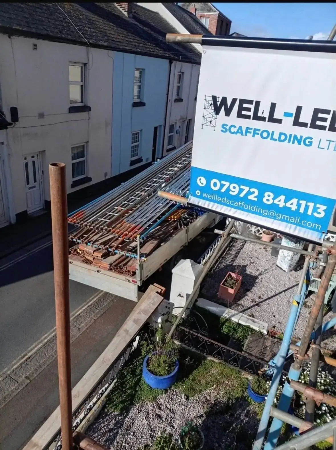 Well-Led Scaffolding lorry loaded with tube and fittings on a terraced street in Exeter, seen from a scaffold carrying the company banner.