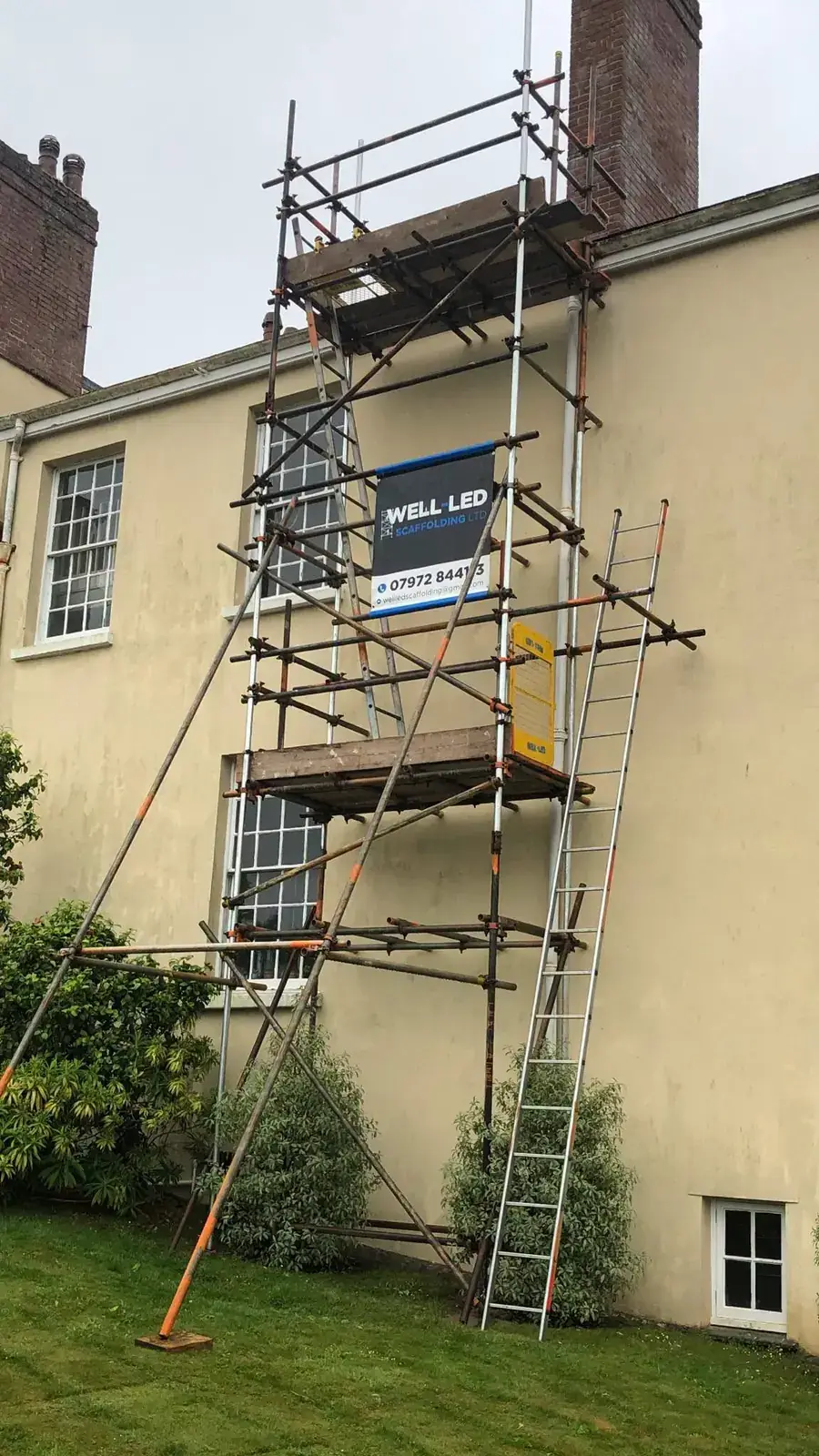 Three-lift tower scaffold against the gable end of a period house in Devon, with ladder access to each lift.