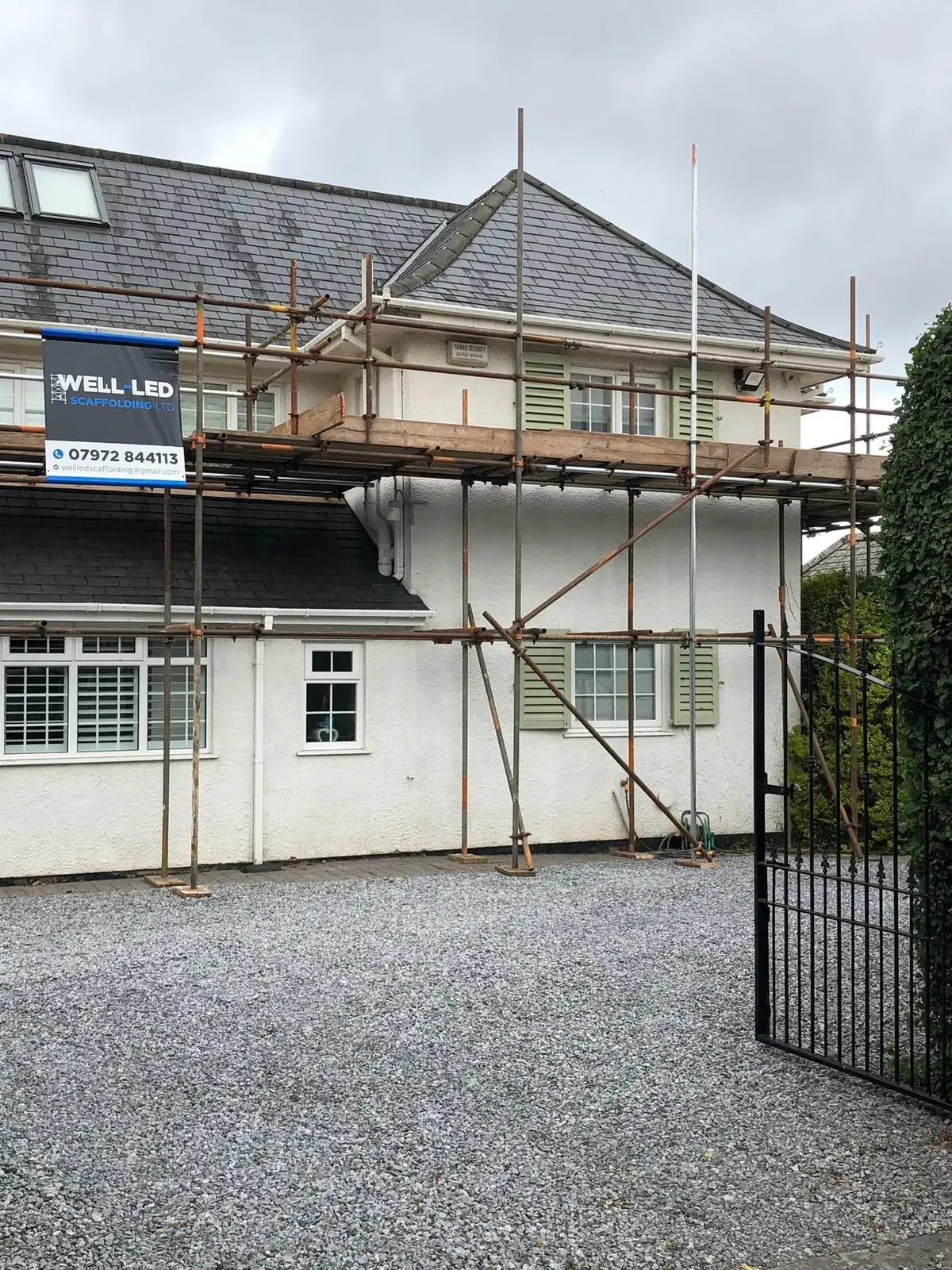 Two-lift access scaffold across the front of a detached house in Devon, with the Well-Led Scaffolding banner in place.